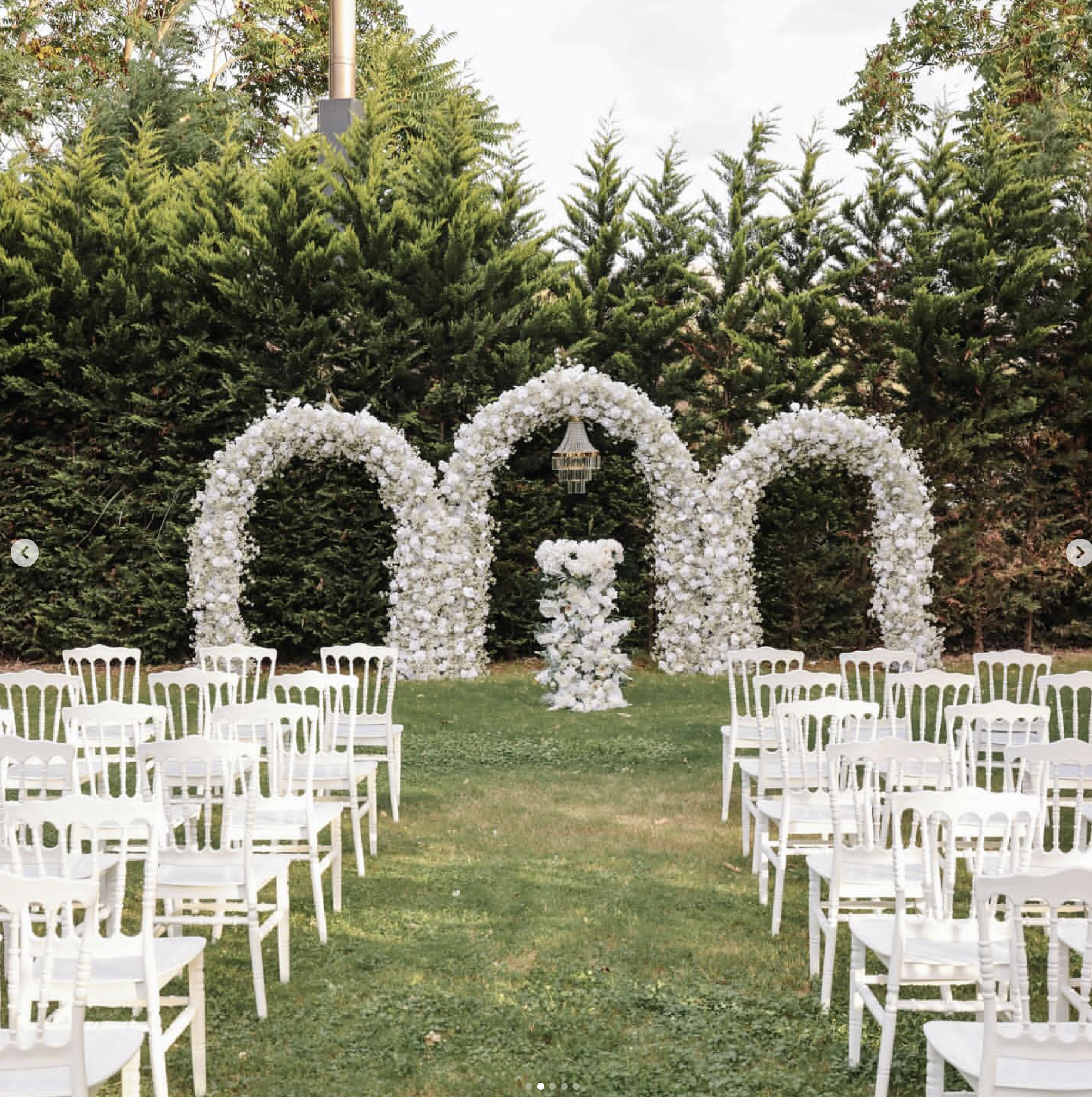 Twin white floral arches with a hanging crystal chandelier over a ceremony aisle